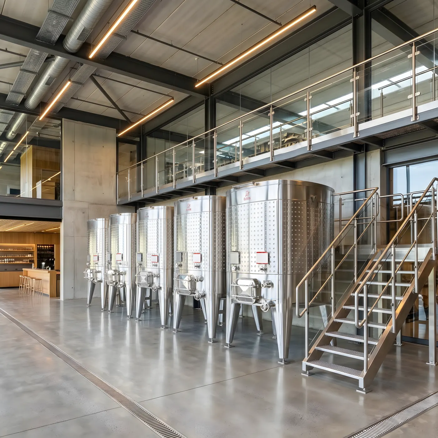 A line of Olavin square fermenters along a winery wall, with the visitor walkway running the length of the room above them