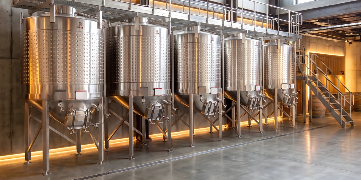 Olavin enclosed conical fermenters on legs along a concrete cellar wall