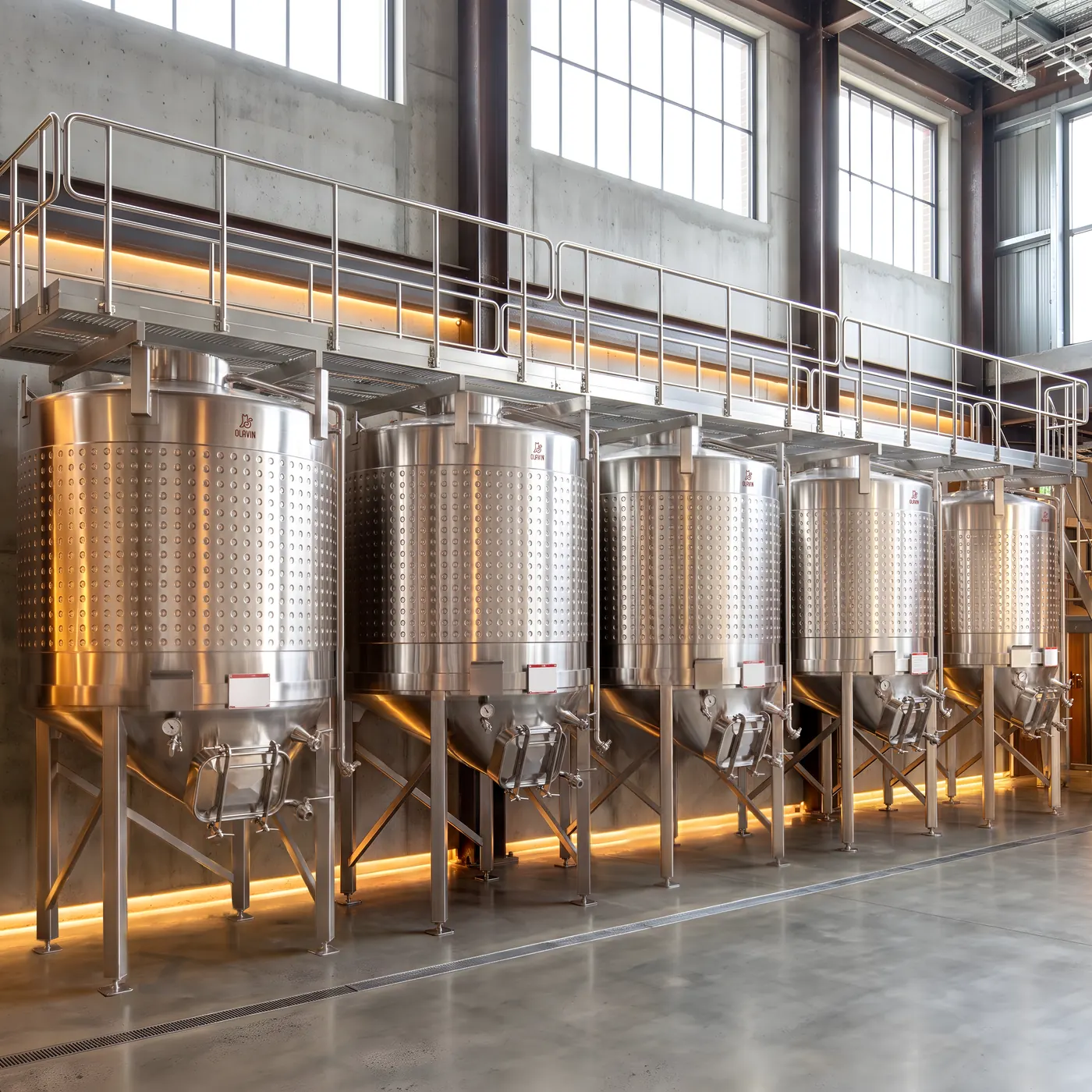 A row of Olavin enclosed conical fermenters along a cellar wall with the service walkway running above them