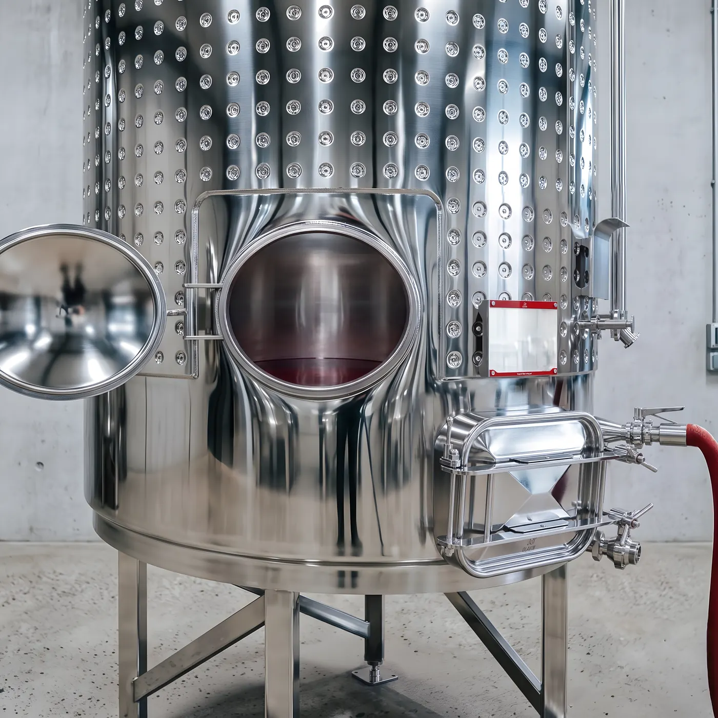 Clear wine being drawn off an enclosed fermenter through the racking valve, with the oval racking door open at the tank base and a red transfer hose connected