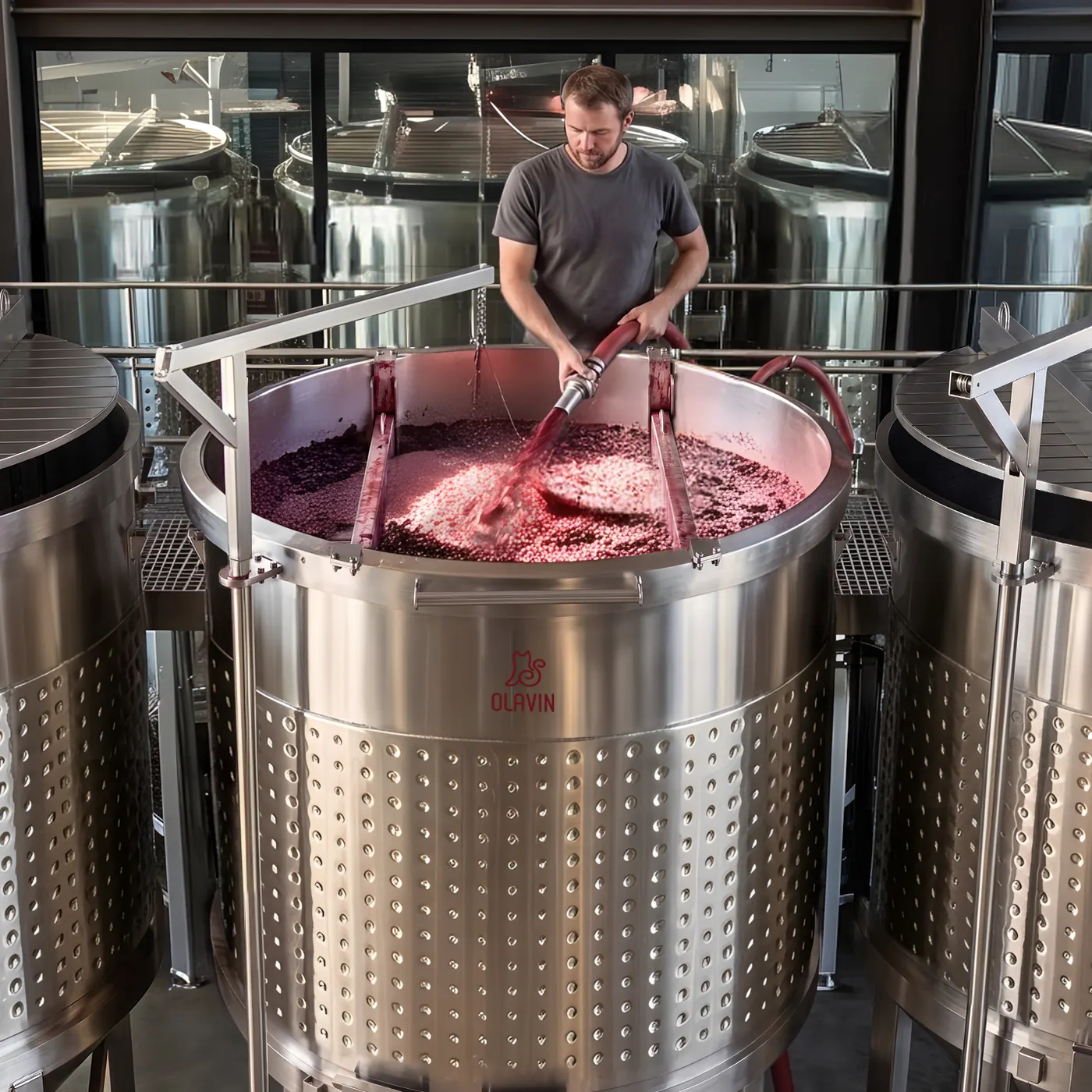 A winemaker running a pump-over from the rim of an open-top conical fermenter, hose in hand and the cap of skins floating in the opening below