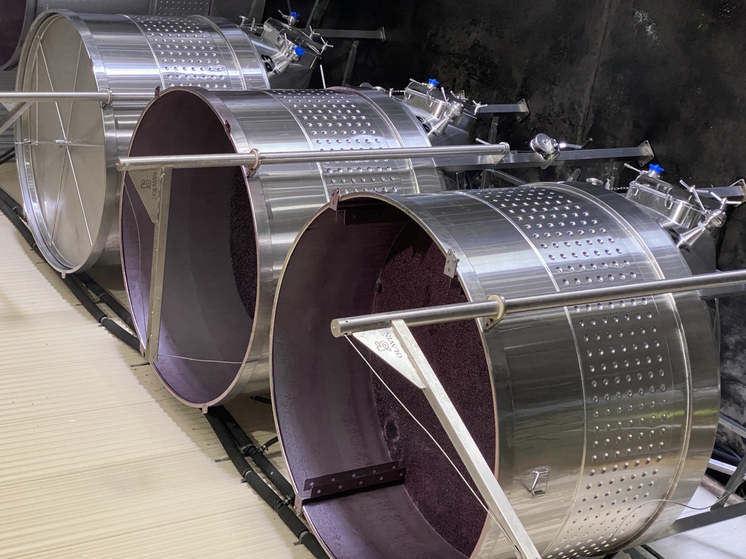 Three Olavin open-top conical fermenters in a row: the two nearest hold fermenting Shiraz under heading-down boards, while the furthest tank has already been closed with an Olavin floating lid.